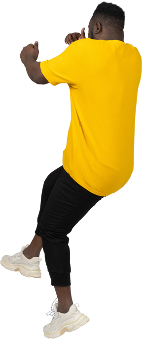Back view of a young dark-skinned man in yellow t-shirt jumping back