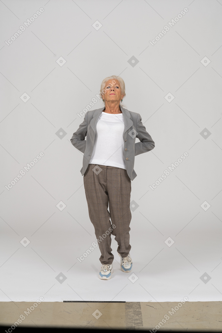 Vista frontale di una vecchia signora in abito in piedi con le mani dietro la schiena