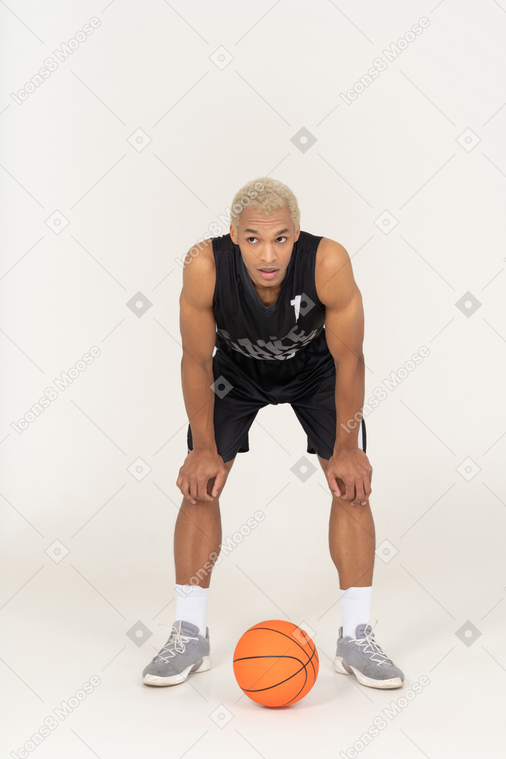 Vista frontal de um jovem jogador de basquete em pé ao lado da bola