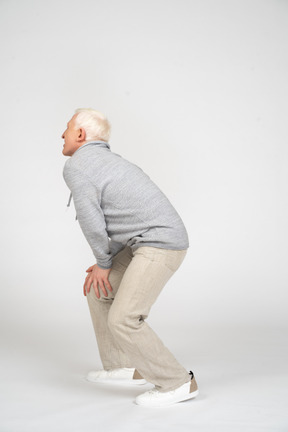 Side view of man standing with his hands on his knee