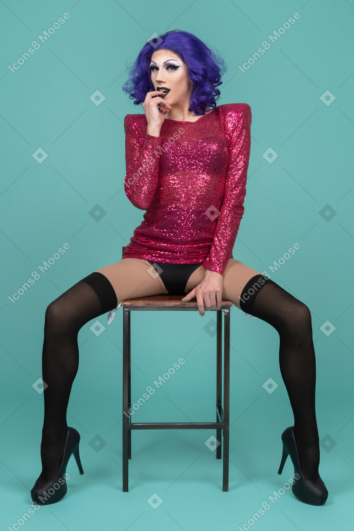 Drag queen mordiendo seductoramente el dedo mientras se sienta en un taburete