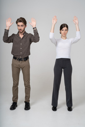 Front view of a young couple in office clothing raising hands