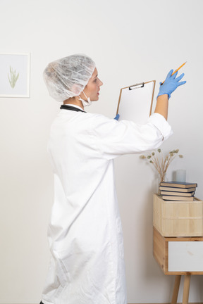 Three-quarter back view of a young female doctor making notes on her tablet