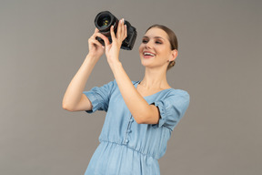 Vista frontal de uma jovem sorridente com vestido azul tirando uma foto
