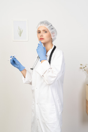 Three-quarter view of a perplexed young female doctor with stethoscope holding thermometer