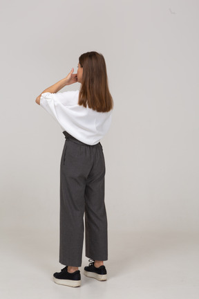 Vista posteriore di tre quarti di una giovane donna in abiti da ufficio che nasconde la bocca