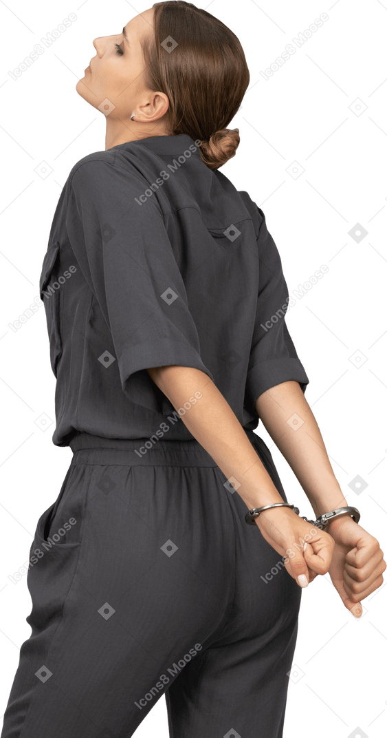 Three-quarter back view of a suffering young woman in a jumpsuit wearing handcuffs