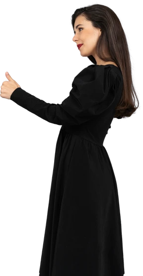 Side view of a smiling young lady in a black dress showing a thumb up