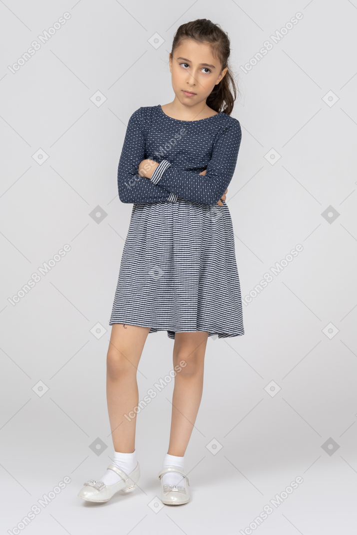 A little girl in a blue dress standing with her arms crossed