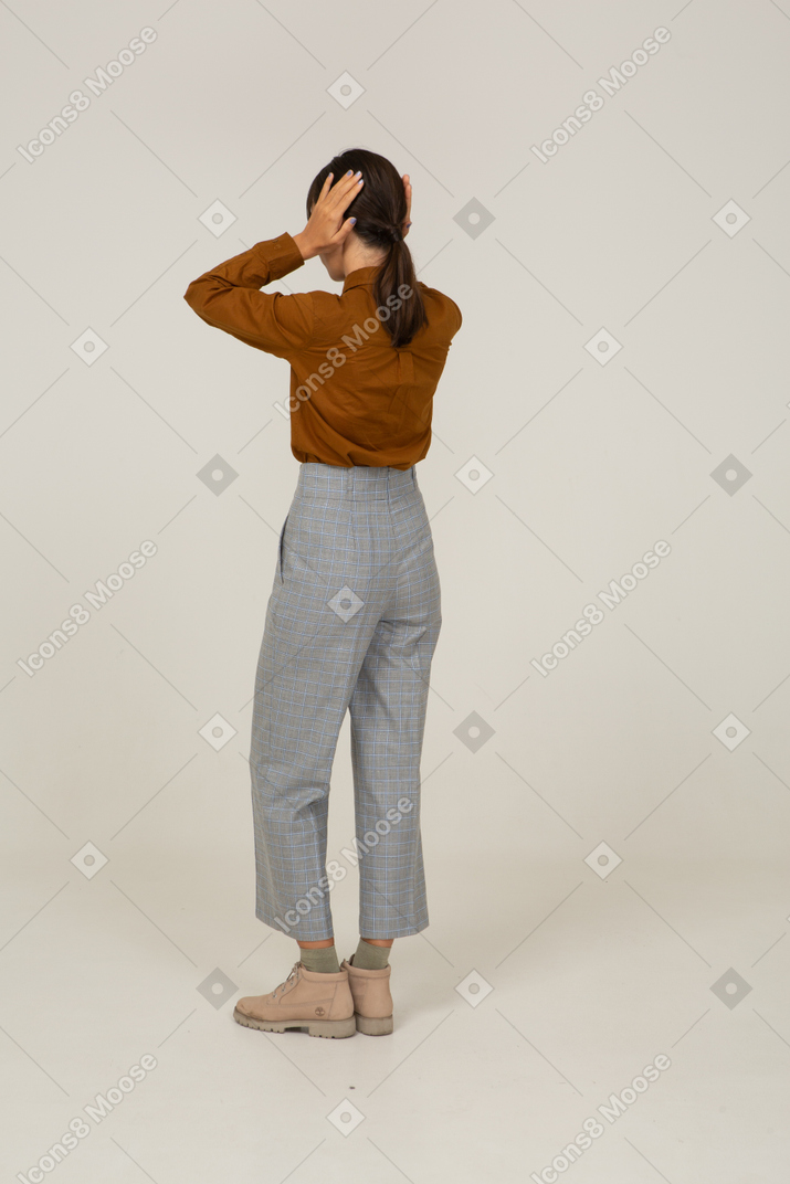 Three-quarter back view of a young asian female in breeches and blouse touching head