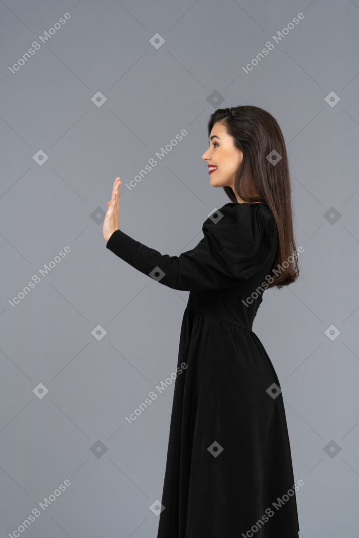 Vista lateral de un saludo sonriente señorita en un vestido negro