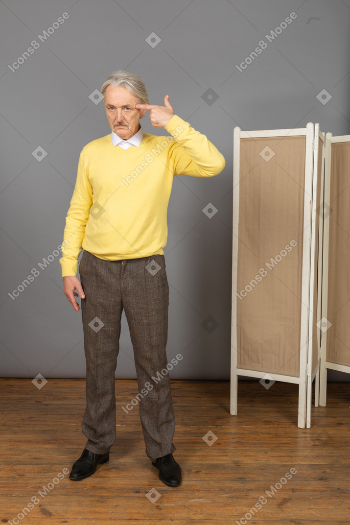 Vista frontal de un anciano pensativo en jersey amarillo apuntando con la cabeza
