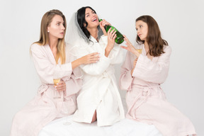 Bridesmaids trying to stop bride from drinking bottle of champagne