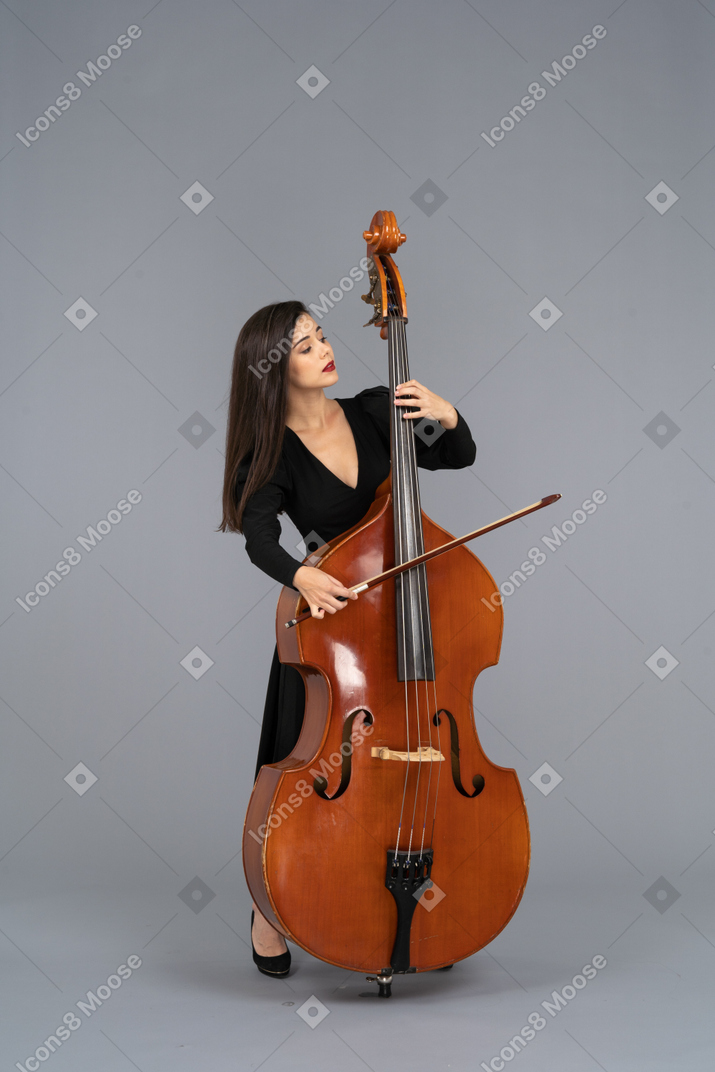 一个年轻的女人，穿着黑色连衣裙，一边看着一边打着弓的双低音的前视图