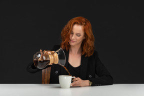 A frontal view of the cute young woman sitting at the table and drinking coffee