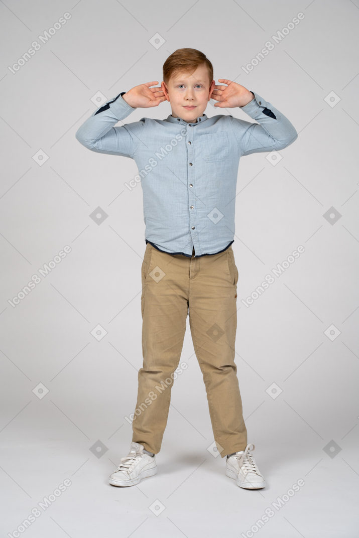 Front view of a cute boy standing with hands on head and looking at camera