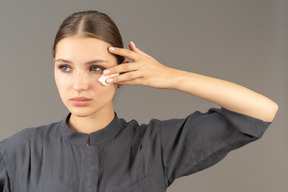 Front view of a young woman in a jumpsuit removing make-up