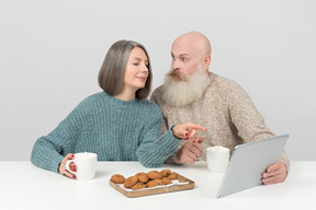 Aged couple having coffee and watching something at tablet