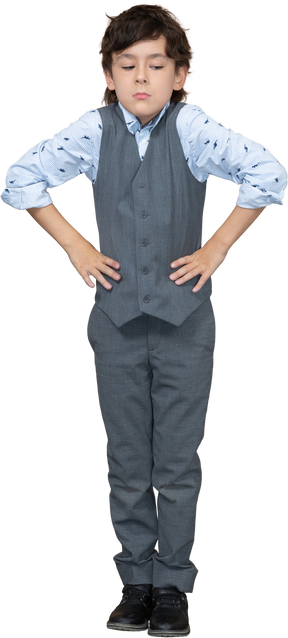 Vista frontal de un niño en traje posando con las manos en las caderas