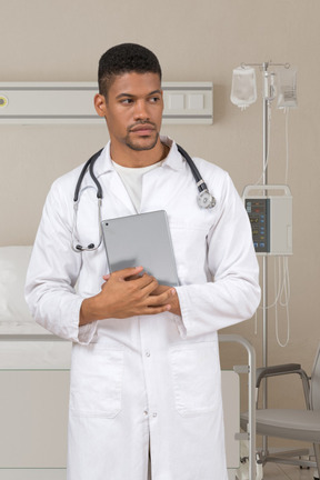 Man in a white lab coat holding tablet and looking aside