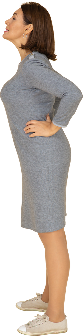 Vista lateral de uma mulher com vestido cinza em pé com as mãos na cintura