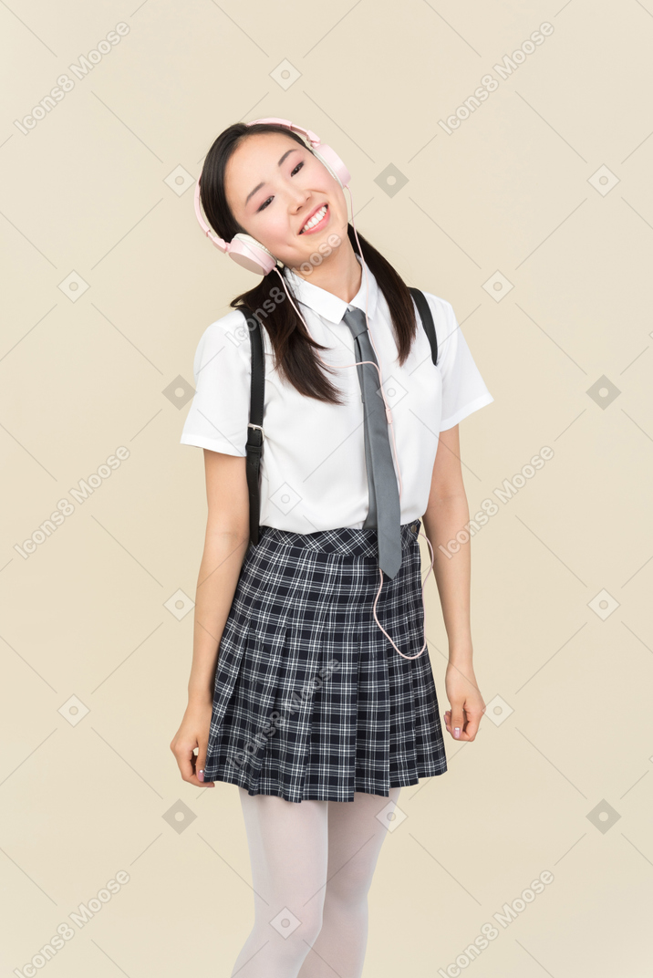 Asian school girl adjusting headphones and looking up