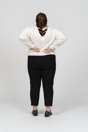 Vista trasera de la mujer regordeta en suéter blanco que sufre de dolor en la espalda baja