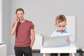 A man talking on a cell phone next to a baby in a high chair