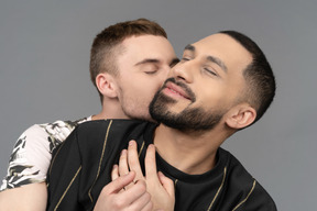 Gros plan d'un jeune homme de race blanche étreignant son partenaire par l'arrière et embrassant sensuellement son cou