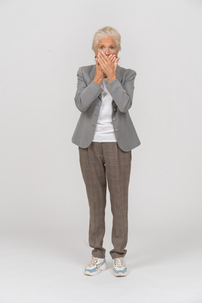 Front view of a scared old lady in suit covering mouth with hands