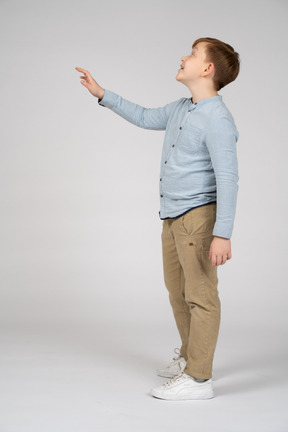 Vista lateral de un niño alegre mirando hacia arriba y saludando
