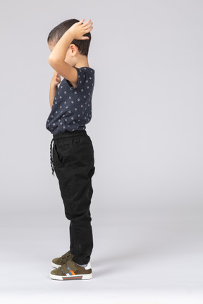 Side view of a boy standing with hand on head