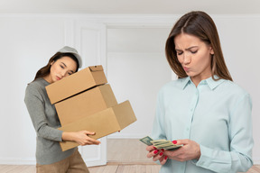 Woman carrying cardboard boxes standing next to a woman counting money