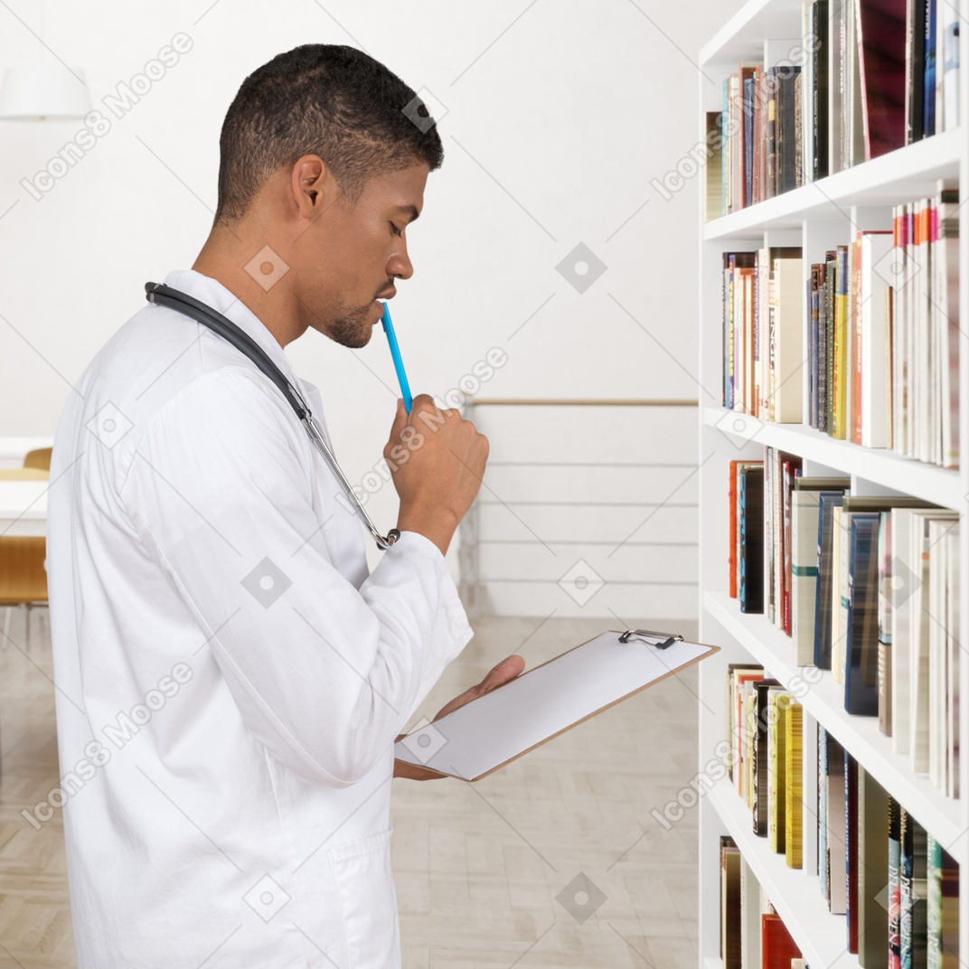 A man standing in front of a book shelf holding a pencil