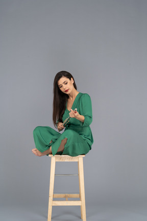 De cuerpo entero de una señorita sosteniendo el clarinete sentada con las piernas cruzadas en una silla de madera