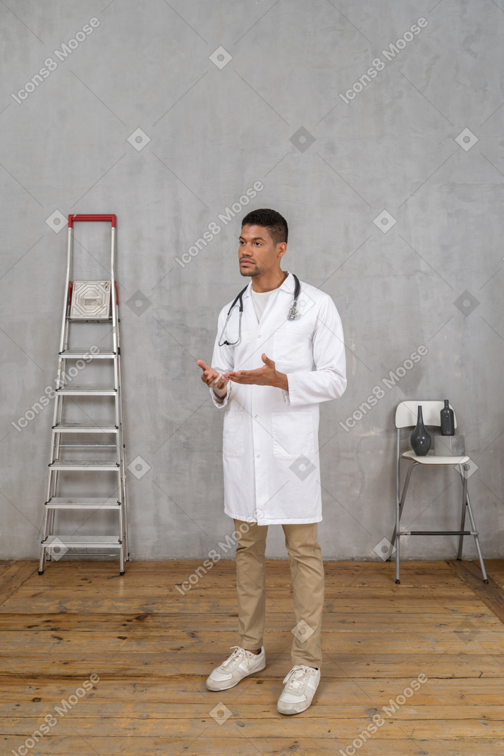 Vista de três quartos de um jovem médico em uma sala com escada e cadeira explicando algo