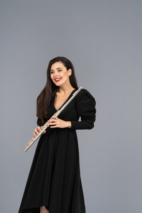 Vista frontal de uma jovem sorridente de vestido preto segurando uma flauta