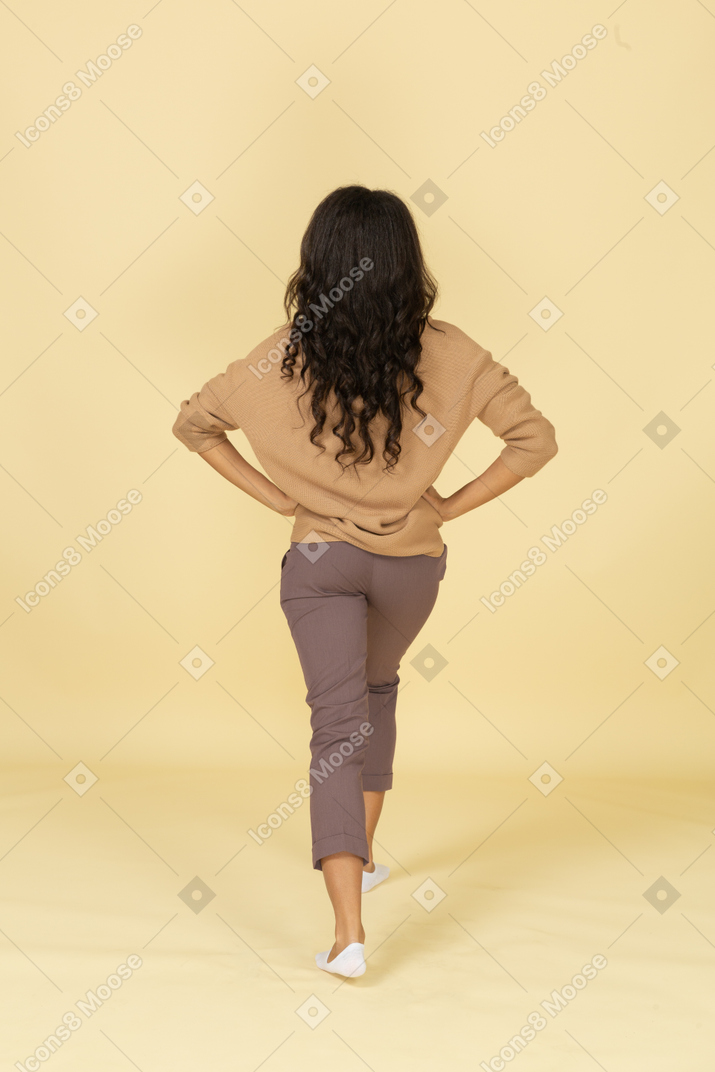 Vista traseira de uma jovem fêmea de pele escura agachada dando uma estocada
