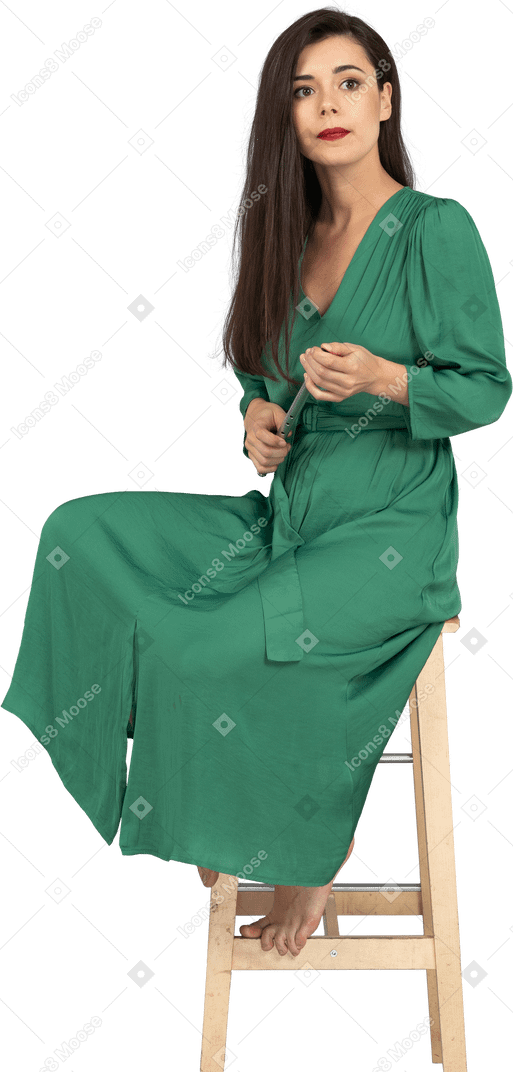 Comprimento total de uma jovem de vestido verde sentada em uma cadeira segurando um clarinete