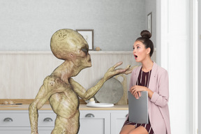 Shocked woman sitting next to an alien in a kitchen
