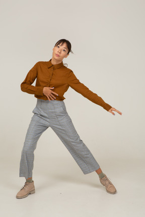 Vista frontal de uma jovem mulher asiática dançando em calça e blusa dando uma estocada