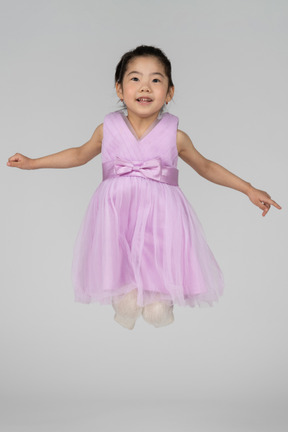 Fille heureuse dans une robe rose sautant avec les jambes pliées