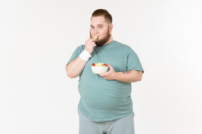 Big guy in sportswear picking salad leaves from the plate