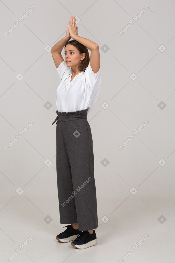 Three-quarter view of a young lady in office clothing holding hands together over her head