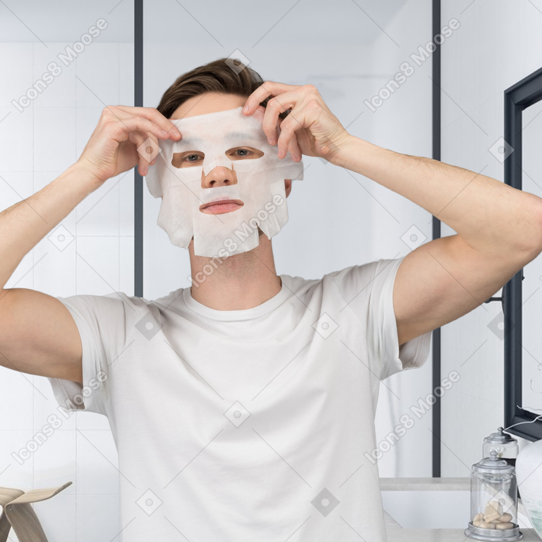 Мужчина надевает тканевую маску в ванной
