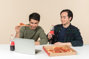 Amigos interraciales comiendo comida chatarra y viendo películas en la computadora portátil