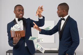 Man in suit throwing money bills and another man pointing at him 