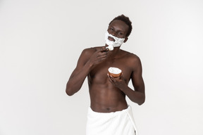 A young black man with a white bath towel around his waist doing his morning routine