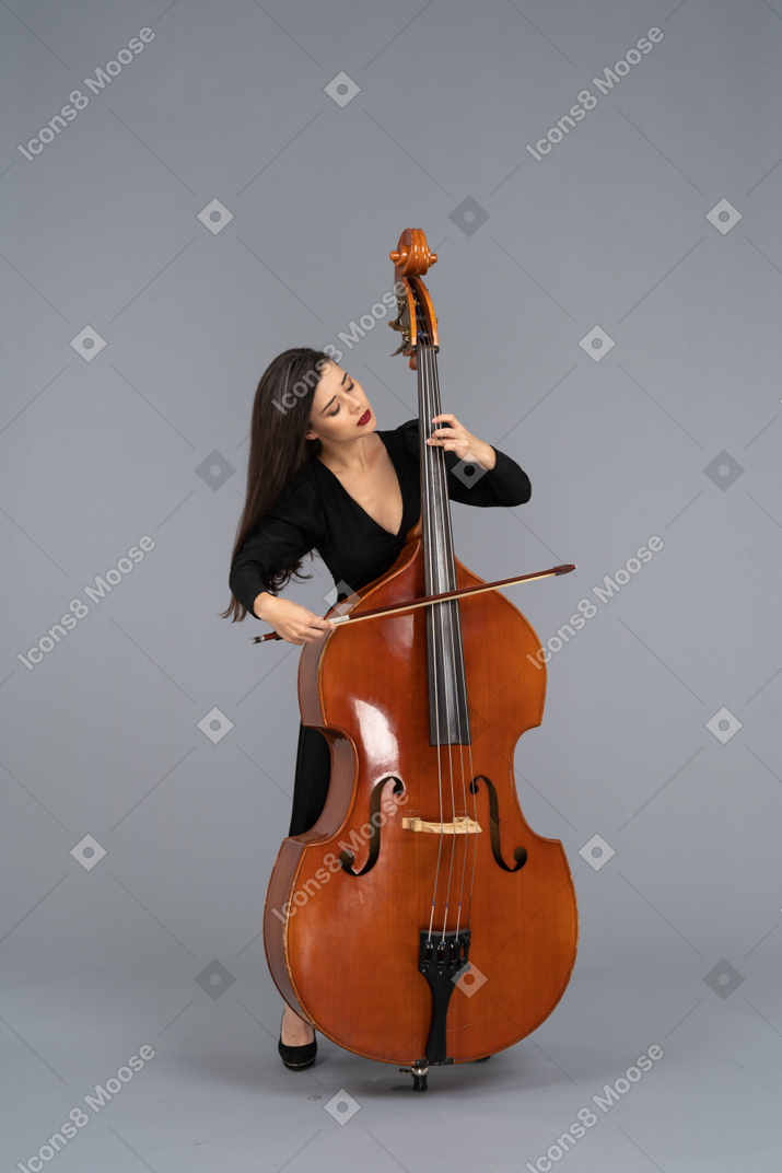 脇を見ながら弓でコントラバスを演奏する黒いドレスを着た若い女性の正面図