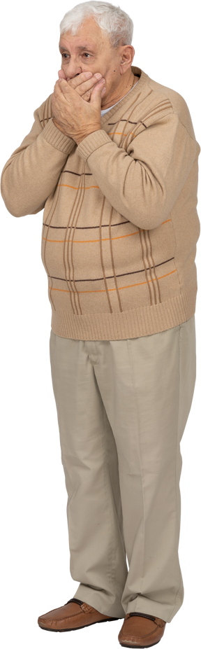 Front view of a scared old man in casual clothes covering mouth with hands